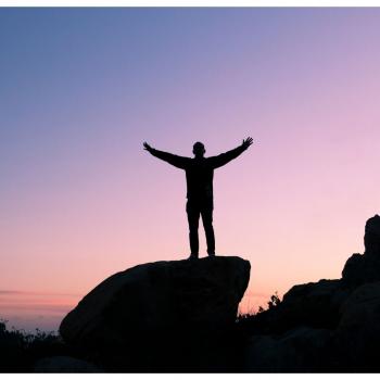 Man standing at the top of a huge rock